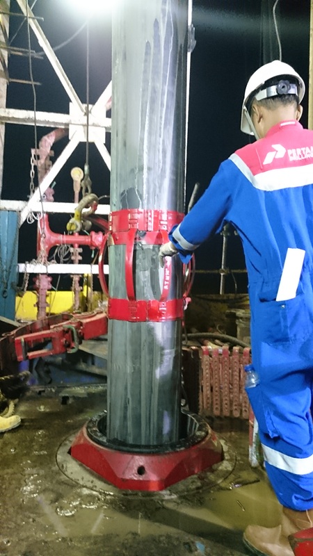 Worker installing a bow-spring casing centralizer on a casing string during drilling operations.